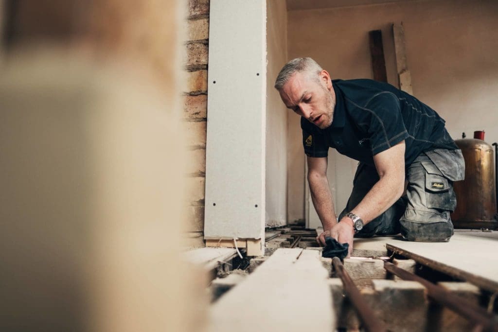 A Heatmyhohm installer about to finish installing the water pipes on a wooden floor in a house.